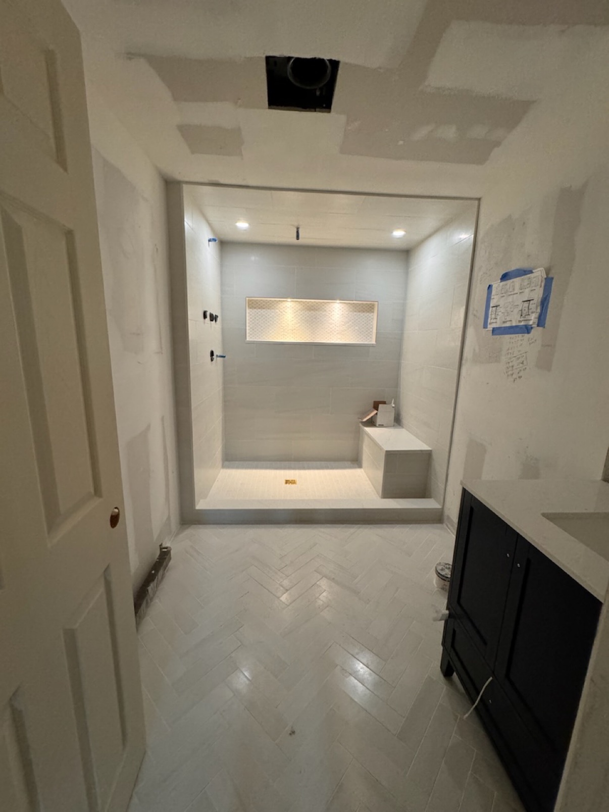 Bathroom with herringbone tile floor, walk-in shower with bench and illuminated niche, and black vanity