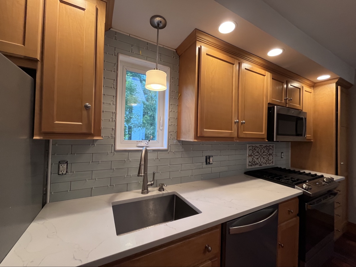Finished kitchen with wood cabinets, white countertop, and gray subway-tile backsplash