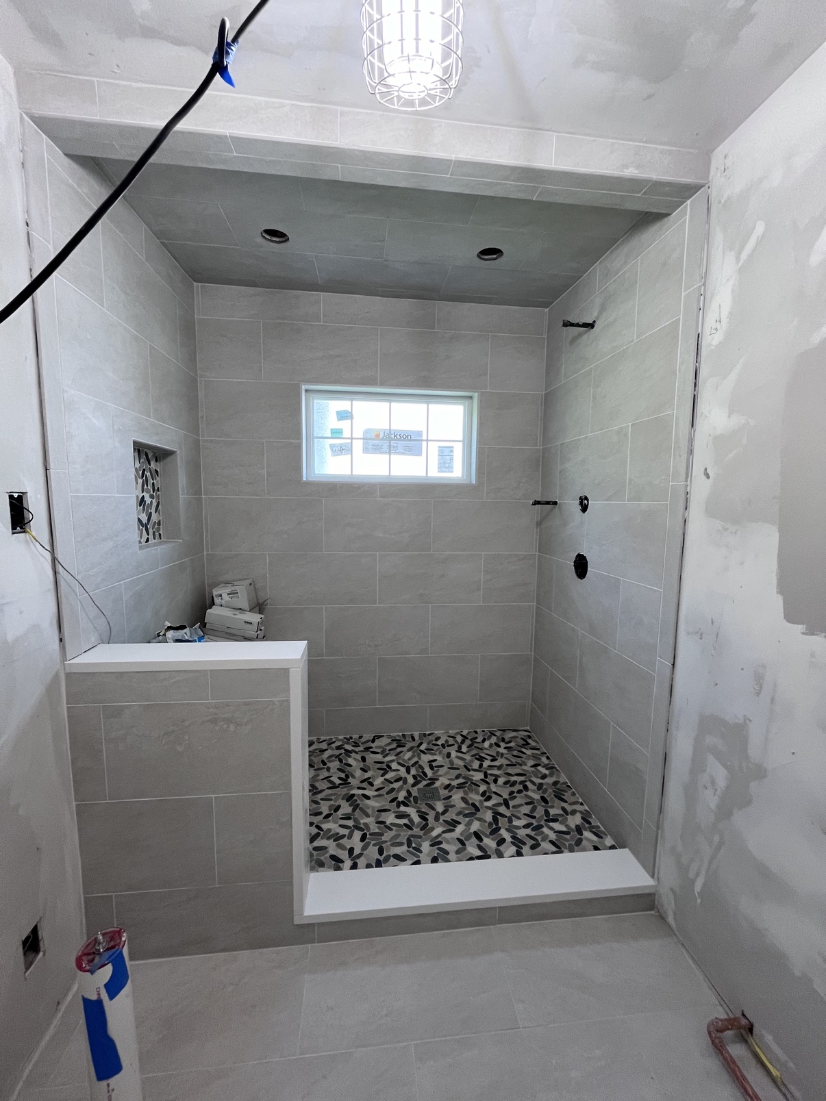 Finished large gray-tile walk-in shower with pebble floor and half wall